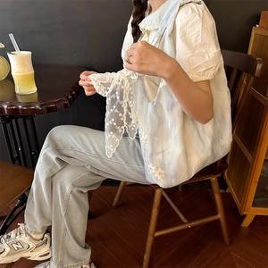 Close-up of light blue floral embroidery on canvas vest with delicate lace-up details