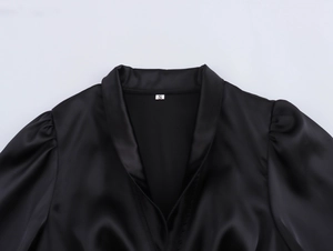 Detail view of V-neckline and puffed sleeve on a black satin dress with size S label