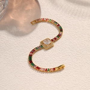 Macro detail of a gold chain bracelet featuring square clear gems and multi-colored stones