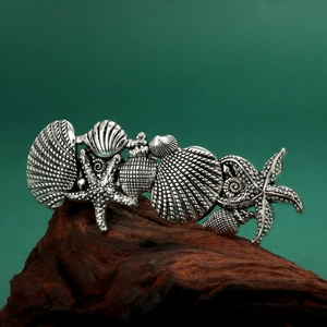 Vintage silver metal starfish and seashell hair clip displayed on textured dark wood