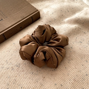Détail d'un chouchou en satin marron avec texture brillante sur tissu en maille beige