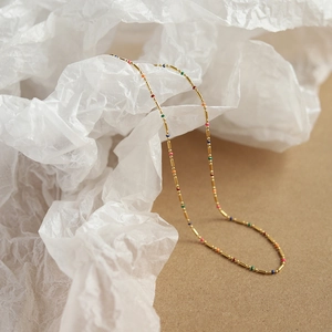 Detailed close-up of a 18K gold plated rainbow bead necklace on a textured background