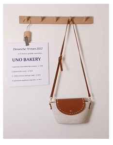 Detail of woven straw shoulder bag with brown leather flap and decorative metal rivets