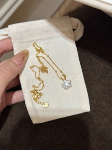 Détail du collier étoile plaqué or avec perle en forme d'étoile sur une pochette en lin