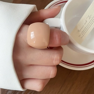 Close-up of minimalist apricot resin square ring worn on hand with soft lighting