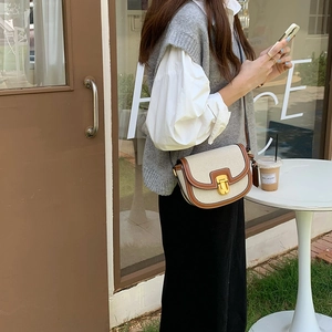 Dettaglio di una borsa a sella beige e marrone con fibbie dorate su una modella