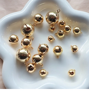 Scattered gold metal bells in various sizes on a white ceramic tray for DIY jewelry projects
