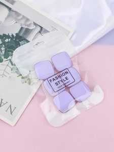 Set of six purple square makeup puffs in transparent packaging over pink fabric