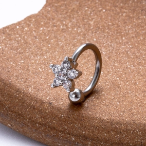 Macro shot of silver stainless steel star piercing jewelry with clear zircons on brown stone