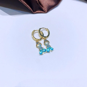 Goldene Creolen mit blauen Zirkonia in Tropfenform auf luxuriösem Seidenhintergrund