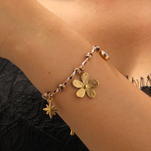Detailed macro view of woven bracelet featuring golden flower and star pendants on wrist