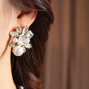 Close-up of elegant gold drop earrings with white pearls and sparkling crystals on model