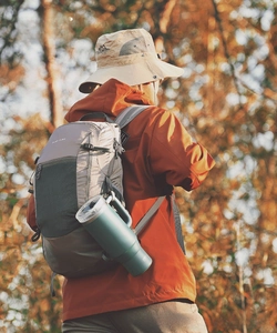 Dark green 40oz insulated tumbler with handle attached to a backpack in forest setting