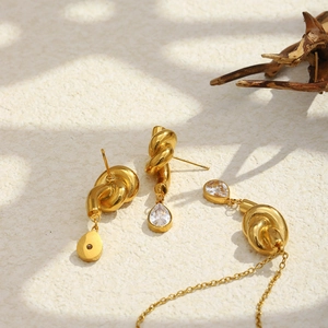 Close-up of gold knotted jewelry set with pear-shaped cubic zirconia under natural light