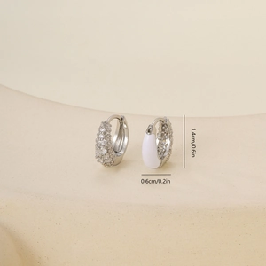 Macro detail of silver hoop earrings with clear cubic zirconia and white enamel texture