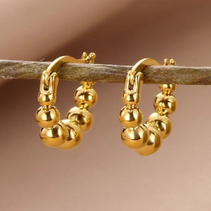 Close-up of 18k gold plated beaded hoop earrings displayed on a natural wooden branch