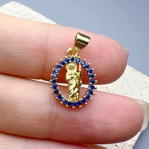 Golden round zircon Jesus pendant with blue stones held against a light stone background