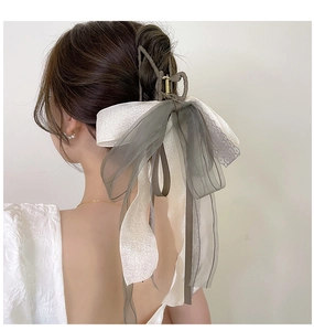 Detail view of large metal shark hair claw with tassel and white ribbon bow on model