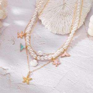 Layered gold necklace featuring starfish, shell and pearl charms on textured stone