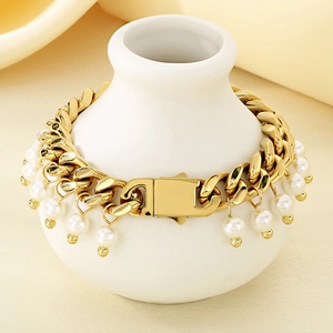 Detail view of a 9mm gold Cuban chain bracelet with hanging white pearls on a ceramic vase