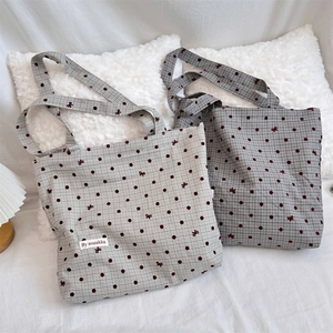 Close-up of canvas tote bag showing red polka dots and bow patterns with woven label