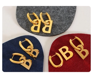Macro shot of gold-plated geometric B earrings on textured felt background cushions