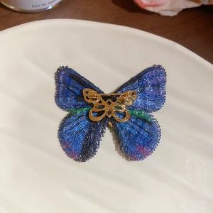 Macro detail of embroidered butterfly brooch with blue gradient texture and gold pin back