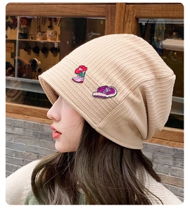Gros plan d'un bonnet en tricot beige orné d'épingles bottes roses et chapeau violet porté