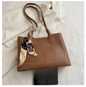 Détail d'un cabas en cuir marron avec surpiqûres et foulard à côté d'un smartphone