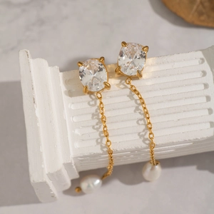 Detail of gold zircon earrings with delicate chain and natural freshwater pearls