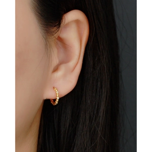 Close-up of a gold s925 silver hoop earring with clear crystals on a model's ear