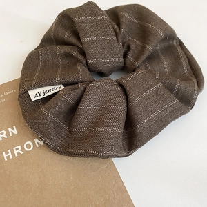 Close-up of brown striped fabric scrunchie with herringbone texture and woven logo tag