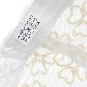 Detail of white heart-shaped hollow lace fabric with 100% polyester care label on the cap