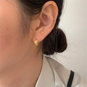 Close-up of a gold seashell striped earring worn on an earlobe in a French minimalist style