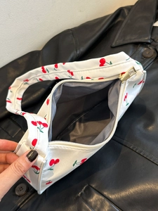 Top view of white nylon handbag with red cherry print showing gold zipper and interior lining