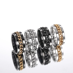 Detail of four spinning Cuban link rings in black, silver and gold finish on white surface