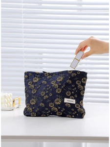 Navy blue canvas makeup bag with gold floral embroidery and hand putting items inside