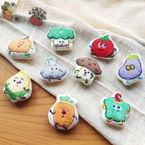 Flat lay of diverse cartoon vegetable plush brooches with detailed embroidery on linen