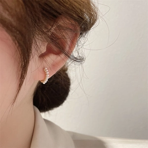 Close-up of minimalist gold pearl hoop earrings worn by a model in a warm white setting