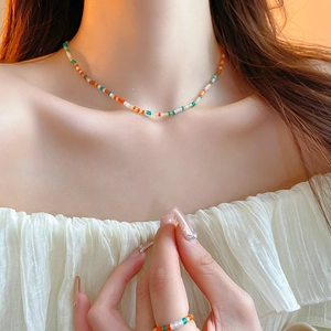 Close-up of colorful beaded necklace and ring set in orange and green worn by a model
