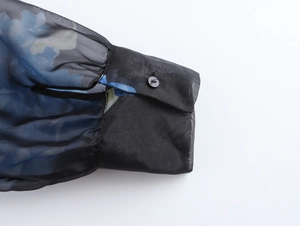 Dettaglio della manica in organza floreale con bottone nero e tessuto blu velato
