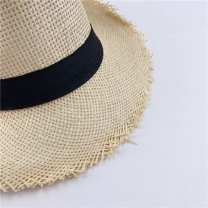 Detail of hand-woven straw fedora featuring raw fringe edges and black ribbon band decoration