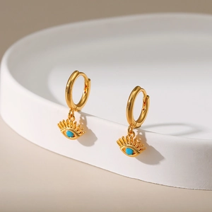 Macro shot of gold hoop earrings with turquoise evil eye charms on a ceramic plate