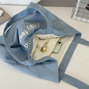 Dettaglio della borsa tote in velluto a coste blu con tasca interna e ricamo bianco
