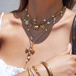 Layered gold necklace featuring heart and cross pendants with pearl beads on female model