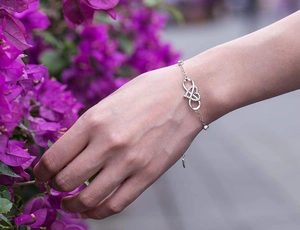 Detail of S925 silver infinity heart bracelet with zircons worn near purple flowers