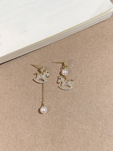 Detailed view of asymmetric horse earrings with gold plating, zircons, and dangling pearls