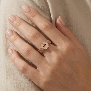 Detail of rose gold mesh band ring featuring a hollow clover charm on a hand