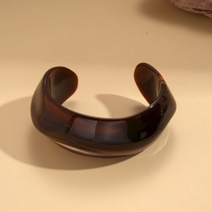 Detail of wide resin open bangle in dark brown featuring a glossy geometric finish