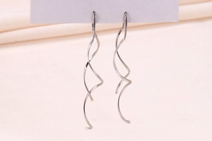 Macro detail of S925 silver spiral earring with long tassels on pink silk background